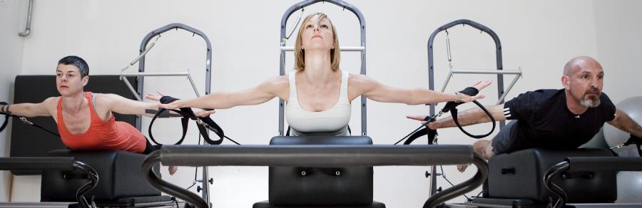 Three clients extending arms on Pilates tower straps over reformers