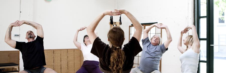 Group class stretching with arms raised overhead in a sunlit studio